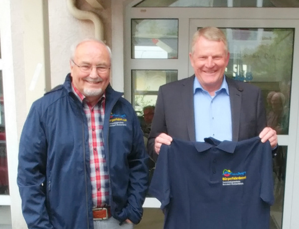 Fahrer Peter Linke (links) und Brgermeister Bernd Brato prsentieren die neue Einsatzbekleidung fr den Brgerfahrdienst der Verbandsgemeinde Betzdorf-Gebhardshain. (Foto: Verbandsgemeinde Betzdorf-Gebhardshain)