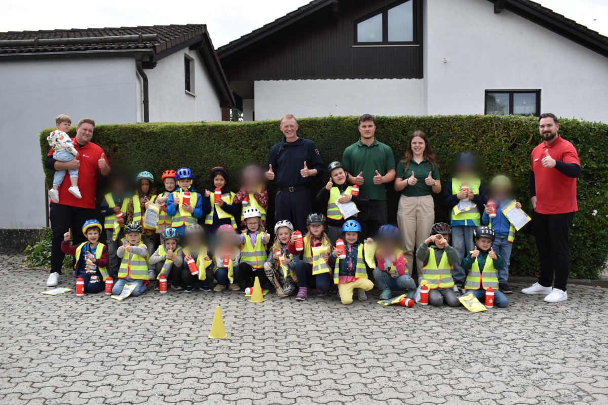 Andreas Neu (links), Leiter FC Westerburg und Wallmerod, mit seinem Sohn und Stellvertreter Marsel Tadic (rechts) mit den Kita-Kindern, deren Erziehern und dem Vertreter der Polizei nach erfolgreichem Verkehrssicherheitstraining auf dem Parkplatz der Naspa in Wallmerod. Foto: Lena Gotthardt