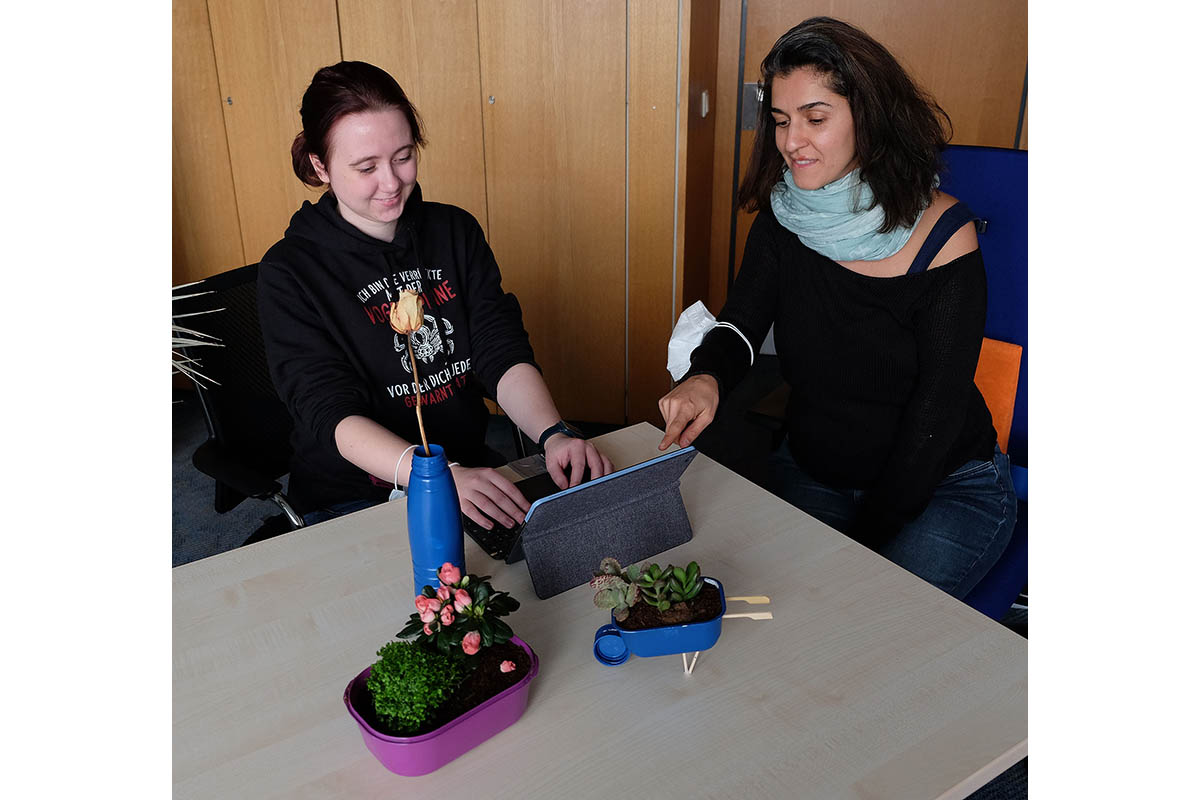 Lisa Hfer (links) und Dr. Zuhal Gltekin blicken auf eine Deko-Schubkarre, die aus einer Butterdose, aus Flaschendeckeln und Schaschlikspieen gefertigt wurde; der Blumentopf war einst eine Eisschachtel, die Vase eine pfandfreie Flasche. Foto: Stadt Neuwied