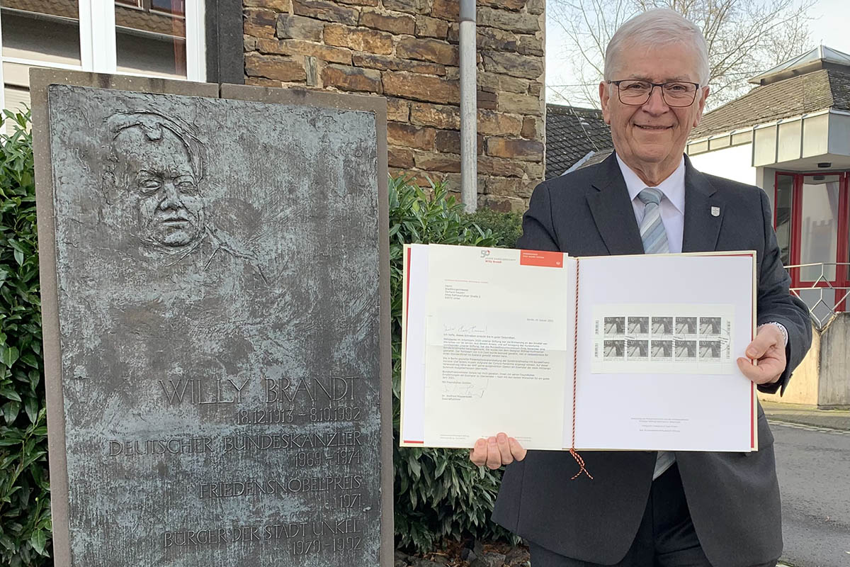 Vor der Gedenktafel des Unkeler Brgers, Bundeskanzlers und Friedensnobelpreistrgers Willy Brandt vor dem Historischen Rathaus der Kulturstadt prsentiert Stadtbrgermeister Gerhard Hausen die stark limitierte Schmuckausgabe-Mappe mit der Sonderbriefmarke anlsslich des 50. Jahrestages des historischen Kniefalls von Warschau. Foto: Thomas Herschbach / Kulturstadt Unkel 