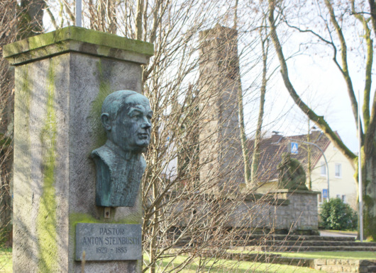 Das Denkmal zu Ehren des Namensgebers Pastor Anton Steinbusch, im Hintergrund das Ehrenmal in der Steinbuschanlage. (Foto: as) 