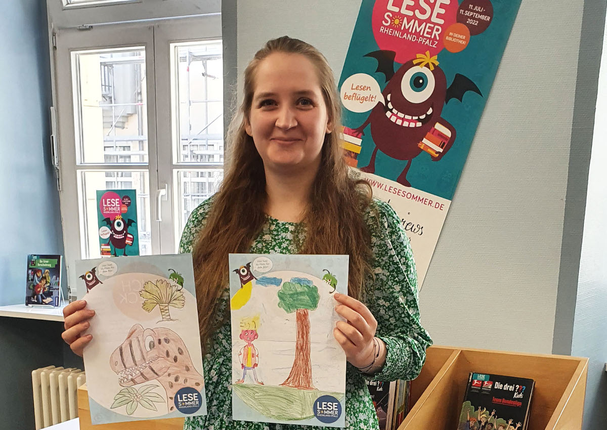 Anna Lenz vom Leitungsteam der Stadtbibliothek zeigt zwei der von Lesesommer-Kindern erstellten Bilder. (Foto: Stadt Neuwied)