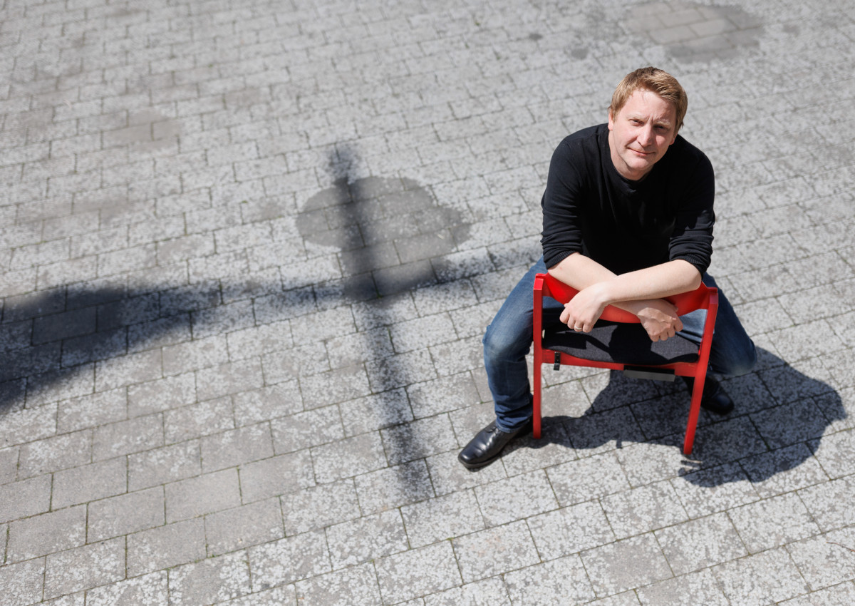Ein Start im Schatten des Kreuzes: Entspannt sitzt Pfarrer Schmitt auf einem der charakteristischen roten Stühle der Evangelischen Kirche Hilgert. (Foto: Peter Bongard)