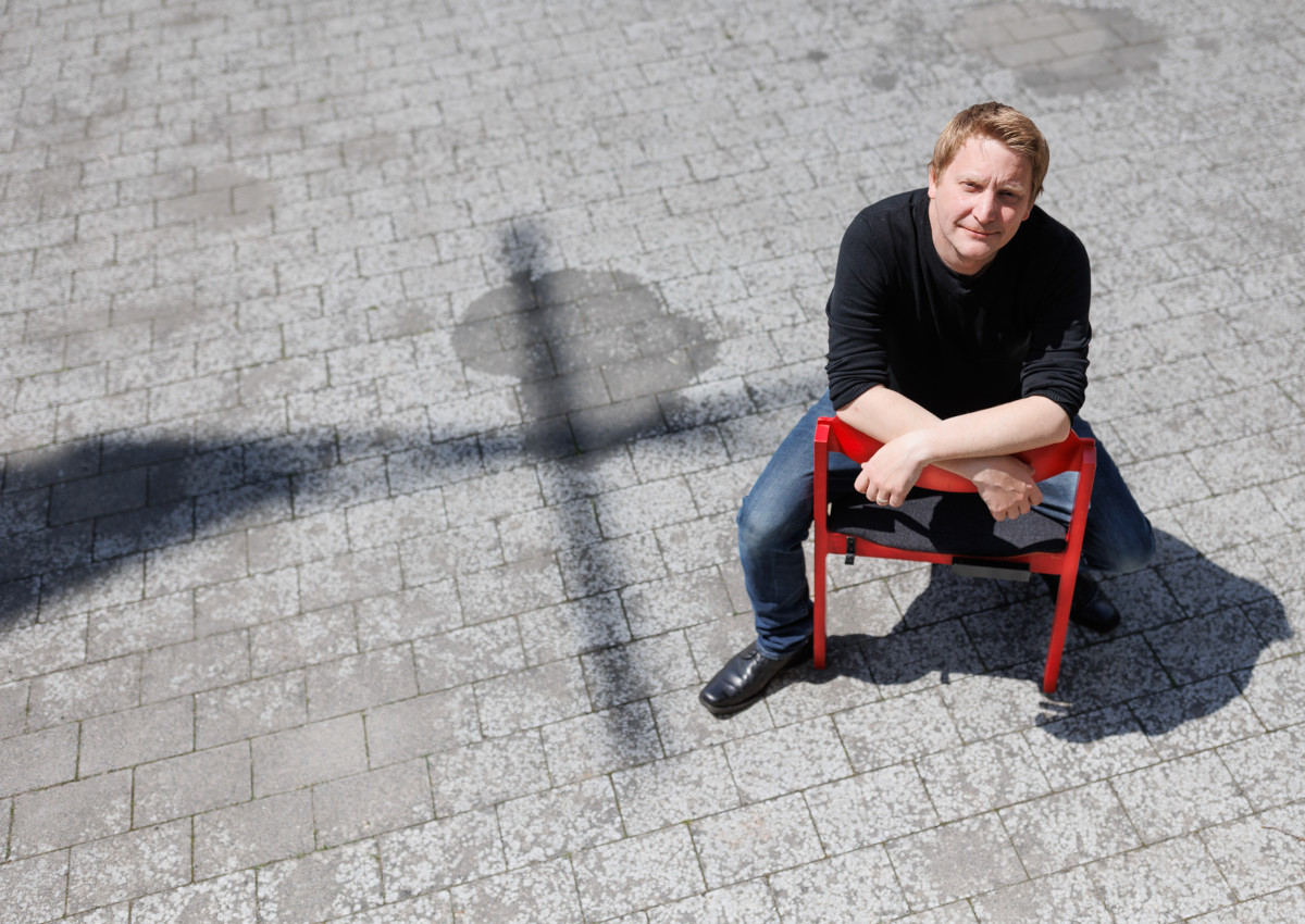 Ein Start im Schatten des Kreuzes: Entspannt sitzt Pfarrer Schmitt auf einem der charakteristischen roten Sthle der Evangelischen Kirche Hilgert. (Foto: Peter Bongard)