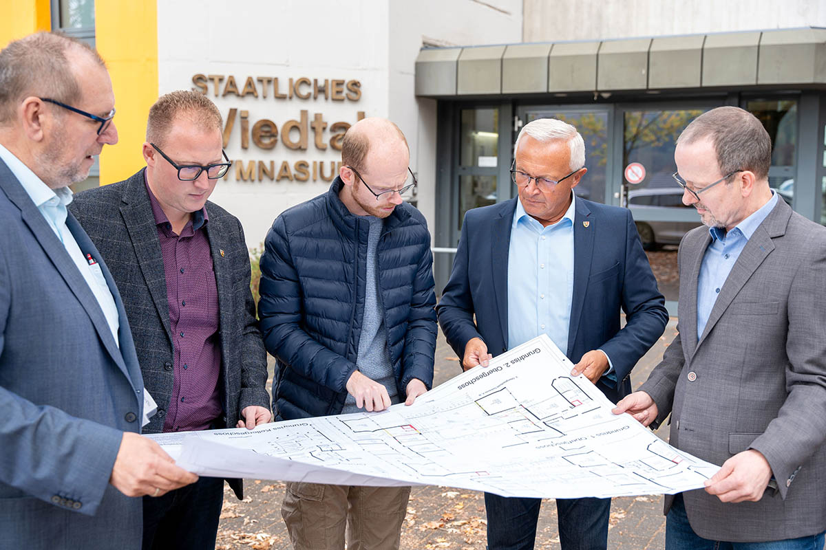 Von links: Rdiger David, Abteilungsleiter des Immobilienmanagements der Neuwieder Kreisverwaltung, der Erste Kreisbeigeordnete Philipp Rasbach, Florian Kropf vom Immobilienmanagement des Kreises, Landrat Achim Hallerbach und Schulleiter Thorsten Mehlfeldt werfen einen Blick auf die geplanten Baumanahmen am Wiedtal Gymnasium in Neustadt/Wied. Foto: Martin Boden / Kreisverwaltung Neuwied.