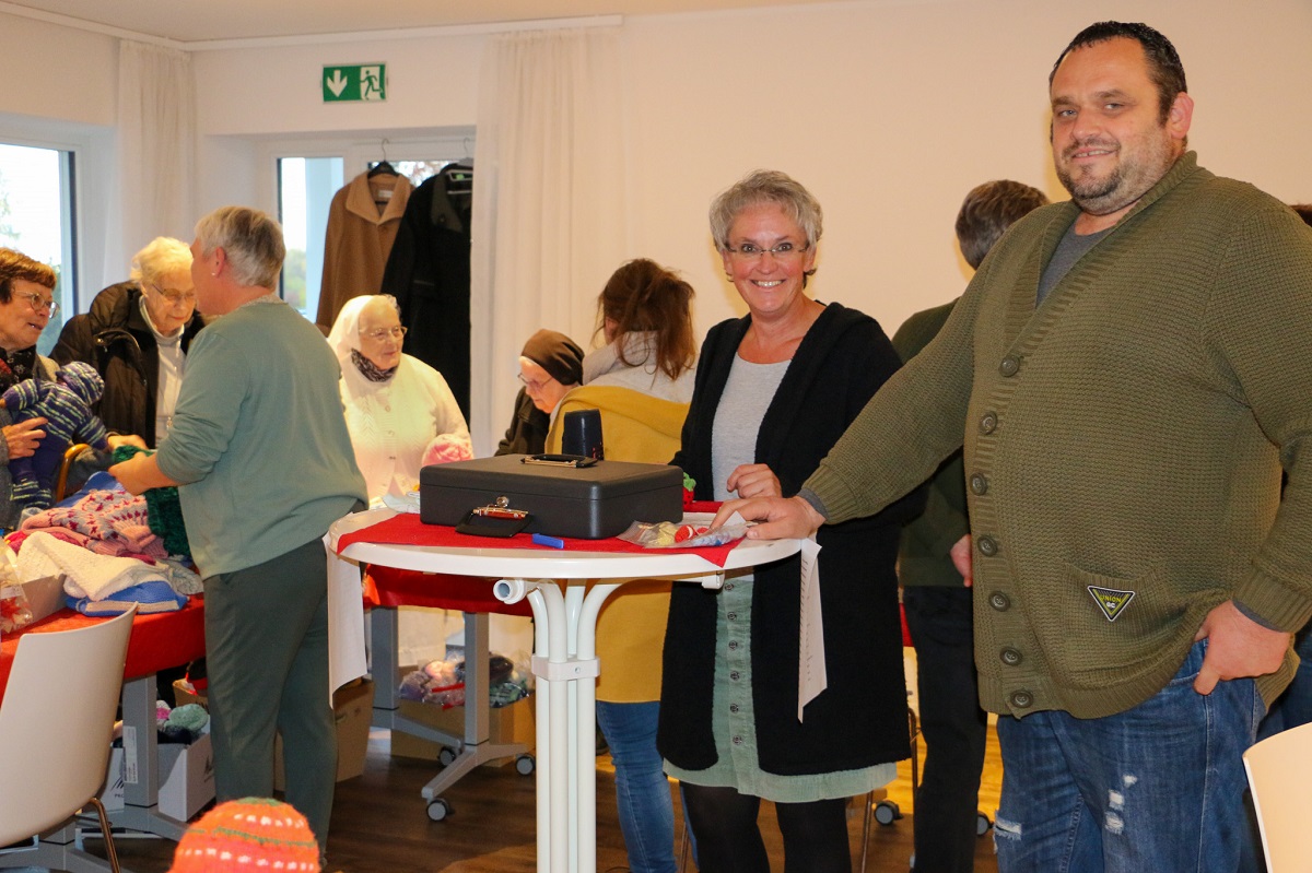 Leitung Eva-Maria Hebgen, stellvertretende Leitung Peter Held, inmitten der Strickwarenspenden, die von den Besuchern des Abends mit viel Freude gekauft wurde. (Foto: DGKK)