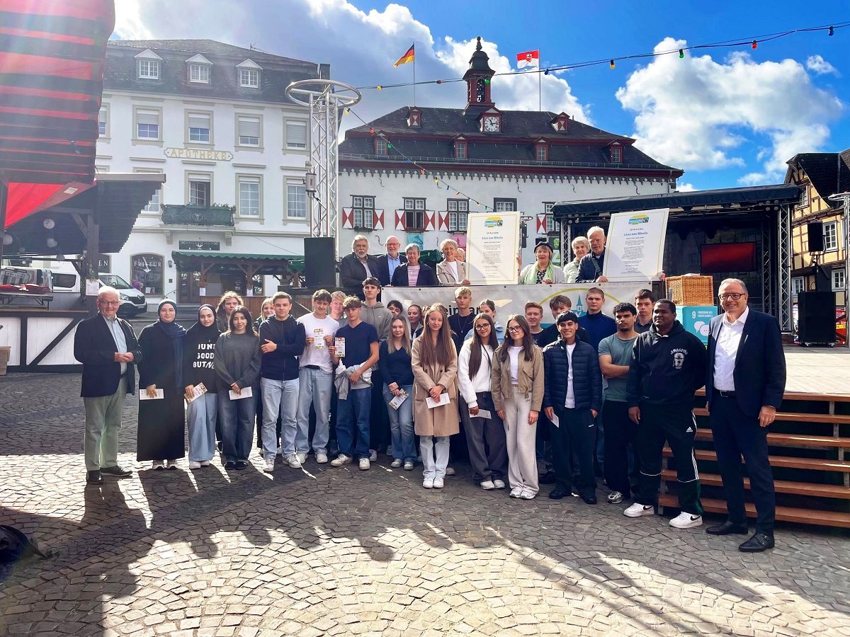 Das Foto zeigt die Schler der Robert-Koch-Schule vor dem Start der Stadtrallye zusammen mit Stadtbrgermeister Helmut Muthers (rechts), dem Sprecher der Fair Trade Steuerungsgruppe Hans-Joachim Schmitz (links) und auf der Bhne mit Mitgliedern der Fair Trade Steuerungsgruppe und des Weltladens. (Foto: Caroline Fritzen, Tourist-Information Linz)
