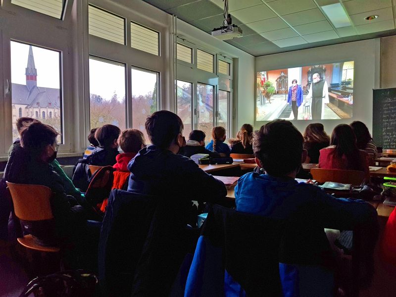 Via Beamer sehen die Schlerinnen und Schler des Privaten Gymnasiums, wie das Friedenslicht von Betlehem in die Basilika, die man live auch rechts im Foto sieht, einzieht. Der Gottesdienst steht als Download auf der Schulhomepage bereit. Fotos: Christian Pulfrich/PGM