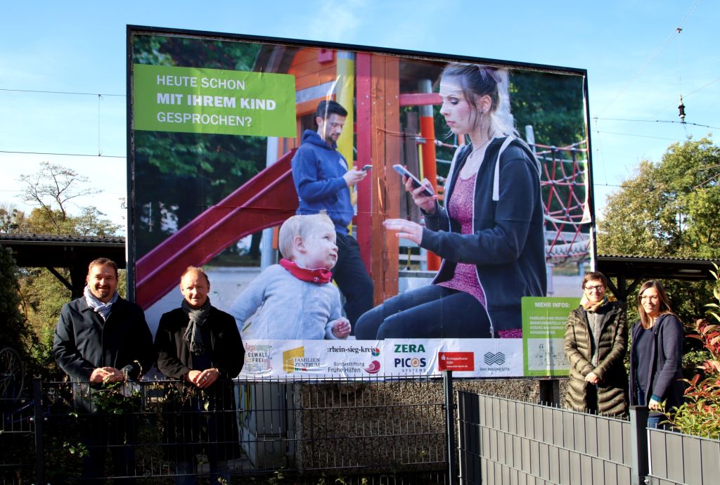 Am Bad Honnefer Bahnhof wirbt ein Plakat fr das Prventionsprojekt FAMILIE DIGITAL  v. l.: Erster Beigeordneter der Stadt Bad Honnef Holger Heuser, Leiter der Familien- und Erziehungsberatungsstelle Jrgen Scheidle, Tatjana Luberg (FEB) und Carin Bierbrauer (FEB). Foto: privat