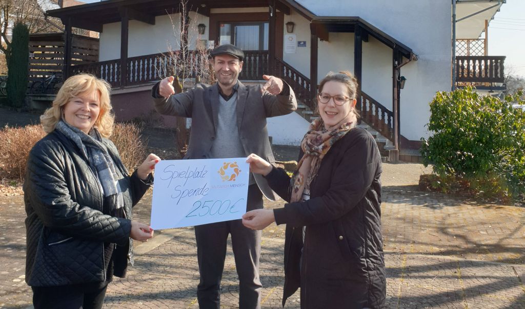 Sabine Klein (l.),  Vorsitzende des Clubhilfswerks berreicht einen symbolischen Scheck an Lara Hbinger (r.), Einrichtungsleiterin der Mutabor Wohngruppen Nister, auf der geplanten Spiel- und Freizeitflche vor dem Haus. Mittig dahinter zeigt Jrgen Sellge, Grnder und geschftsfhrender Gesellschafter, hocherfreut auf den Scheck. Foto: privat