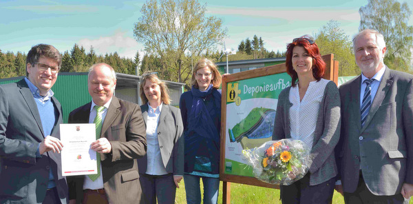 An einem Schild mit einer schematischen Darstellung eines Deponieaufbaus am Beginn des Lernpfades berreichte symbolisch Jan Hendrik Winter (links) die Zertifizierungsurkunde an Werner Schumacher vom AWB. (Foto: tt)